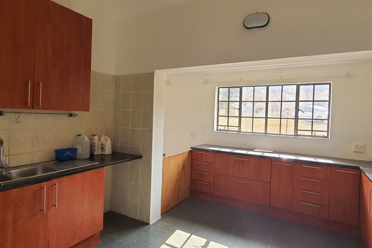 A functional kitchen featuring wooden cabinetry, dark countertops, a gas hob with extractor fan, and a double basin sink with tiled backsplash.