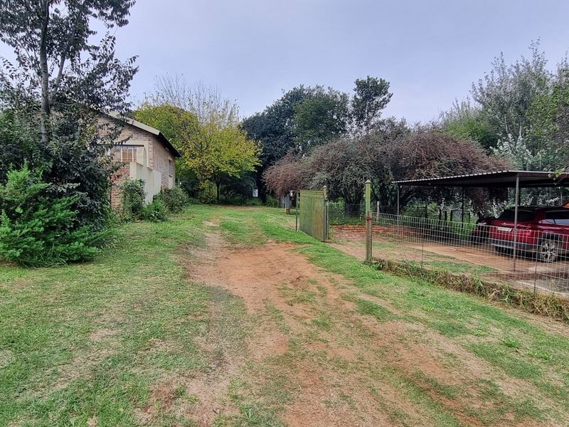 Exterior view of the farm property featuring an unpaved driveway, wire fencing, a metal gate, and a covered carport area.