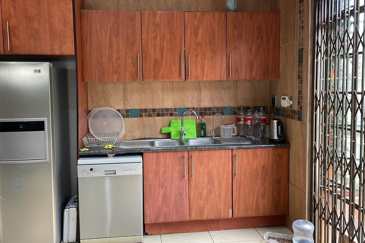 A functional kitchen area featuring wood-look laminate cabinetry, a double sink with mixer tap, tiled backsplash, and an integrated dishwasher.