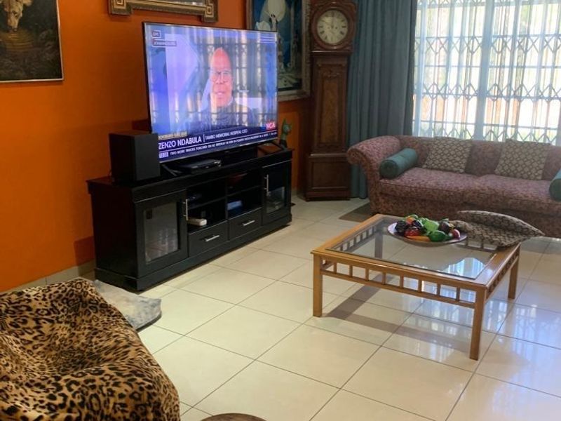 A living room featuring tiled flooring, recessed downlights, and a large window fitted with a security gate and decorative pelmet.