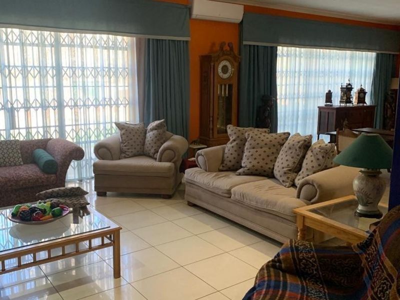 Spacious living room featuring large sliding glass doors with security gates, tiled flooring, and a wall-mounted air conditioning unit.