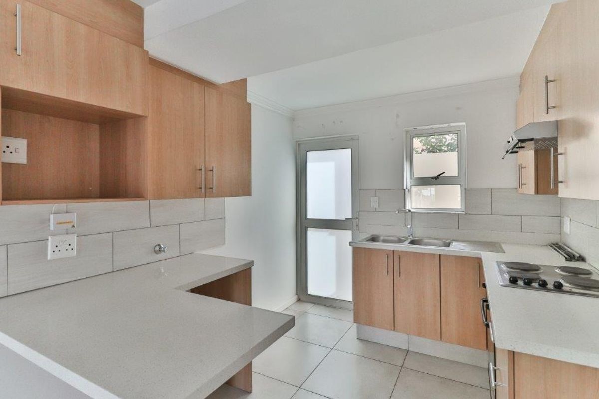 A functional kitchen featuring light wood cabinetry, stone countertops, a built-in hob with extractor, and direct access to an exterior area.