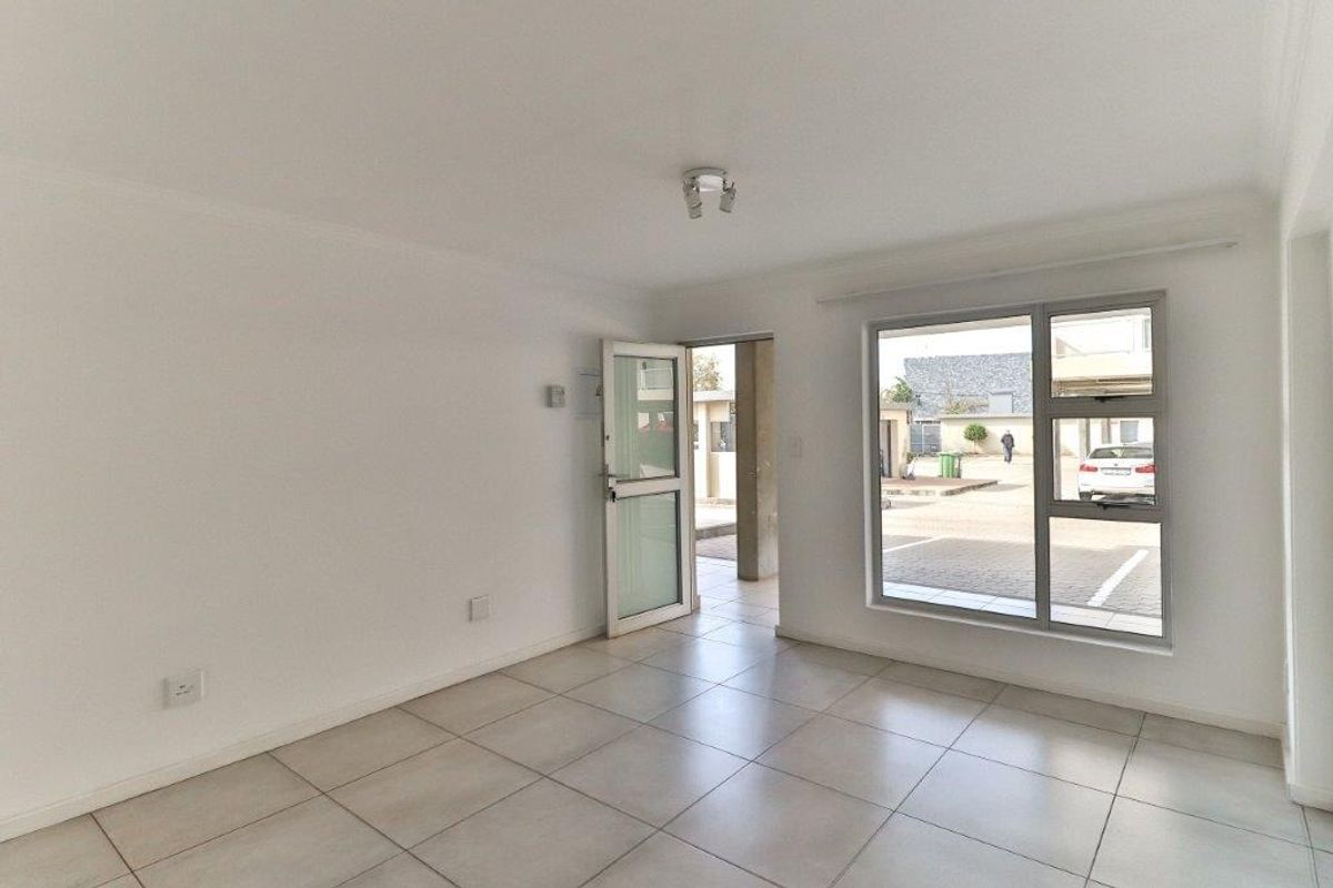 A bright, empty living area featuring neutral tiled flooring, large aluminium-framed windows, and direct access to the exterior.