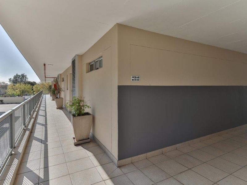 An open-air apartment corridor featuring tiled flooring and a metal mesh safety railing, providing access to residential units.