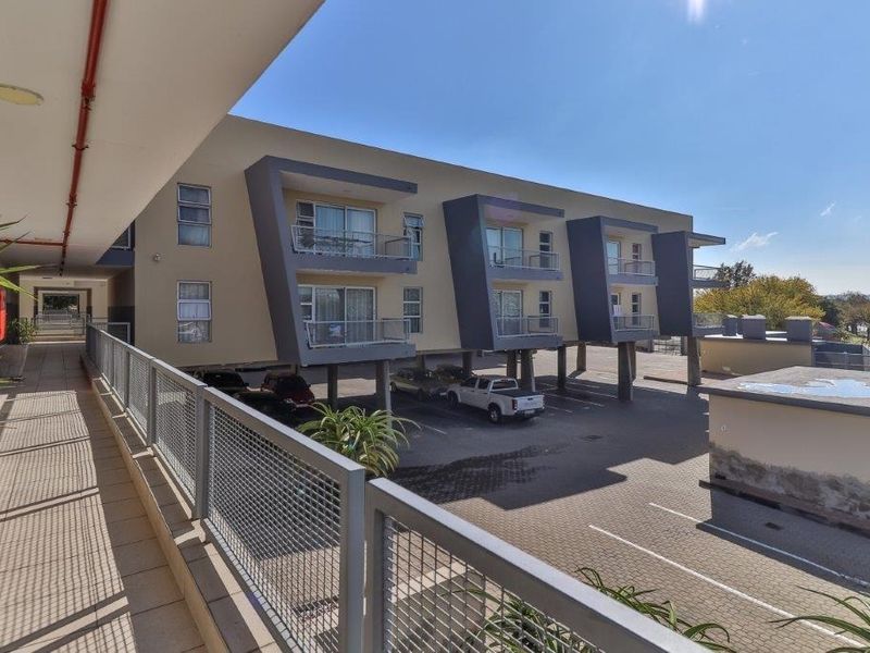 Exterior view of the apartment building featuring a covered walkway, balconies, and a paved ground-level parking area.