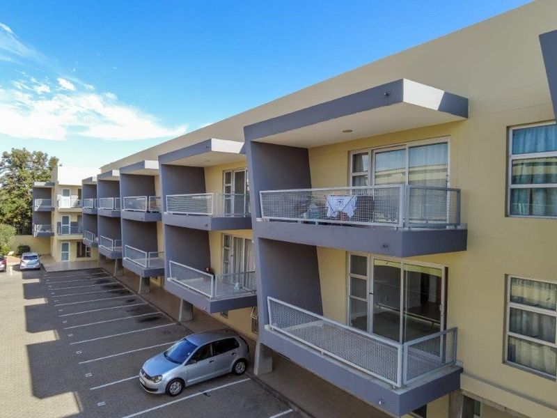 Exterior view of an apartment complex featuring multiple levels of balconies with metal railings and an adjacent paved parking area.