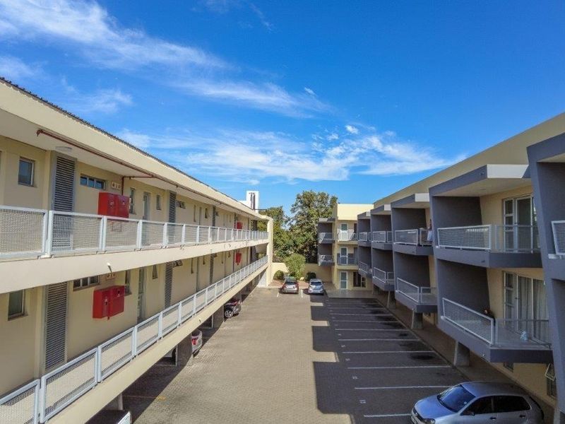 An elevated view of the apartment complex courtyard featuring paved parking bays, multi-level balconies with metal railings, and external building access.