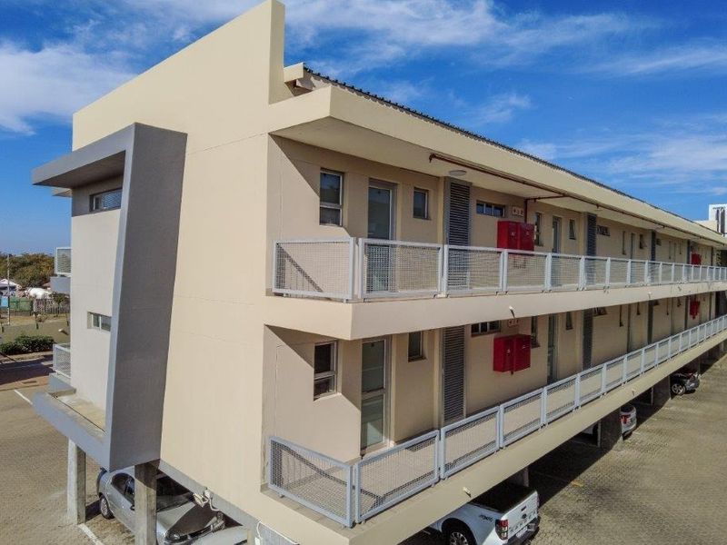 An elevated view of a modern apartment complex featuring multi-level walkways with metal balustrades and covered ground-level parking.