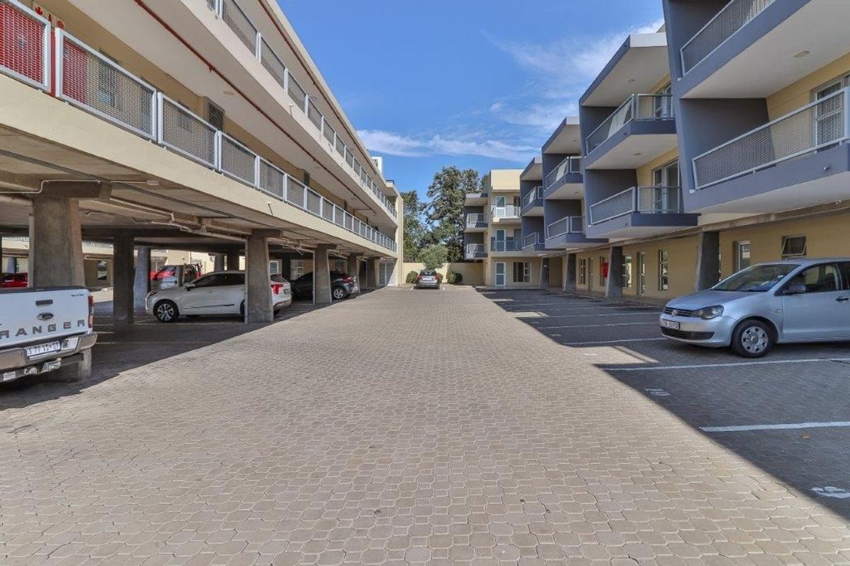 Exterior view of the apartment complex featuring a paved parking area with covered bays and multi-level balconies with metal railings.