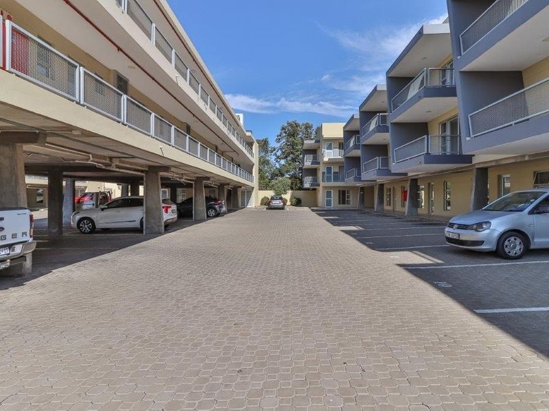 Exterior view of the apartment complex featuring a paved parking area with covered bays and multi-level balconies with metal railings.