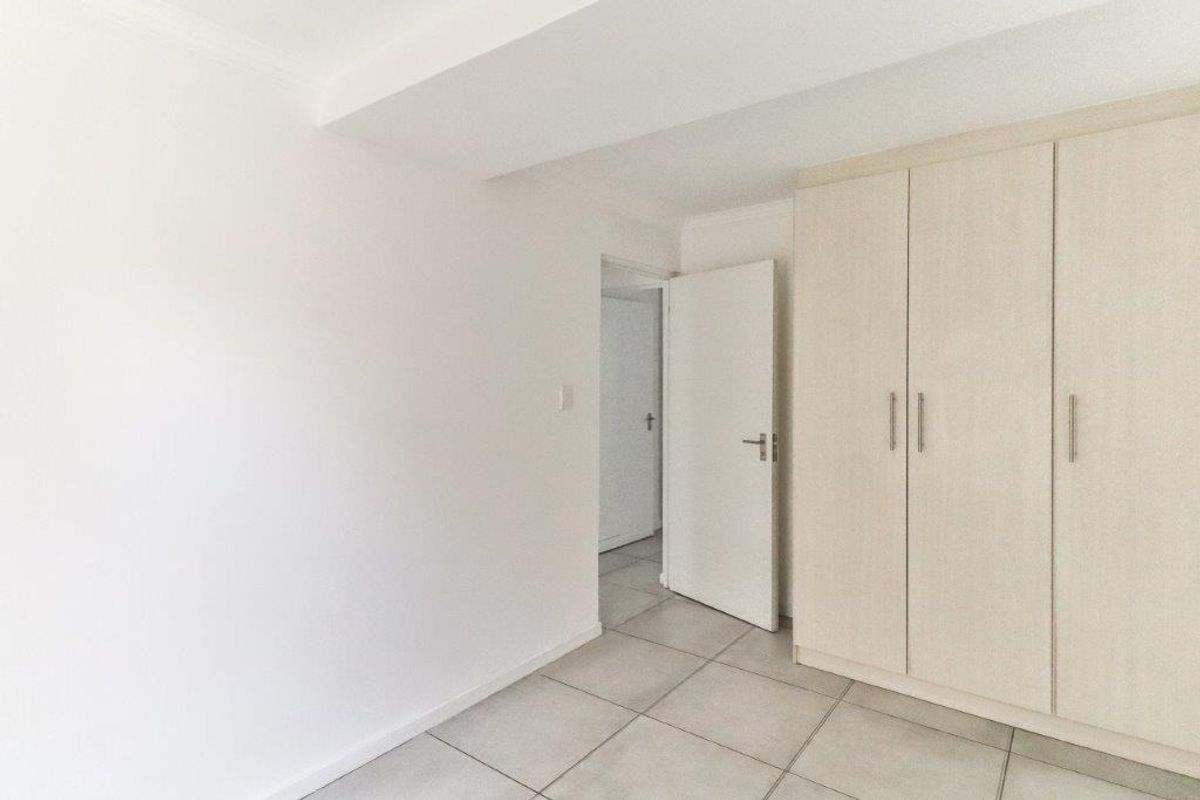 A bright, empty bedroom featuring neutral tiled flooring and a built-in wardrobe with light wood-finish doors.