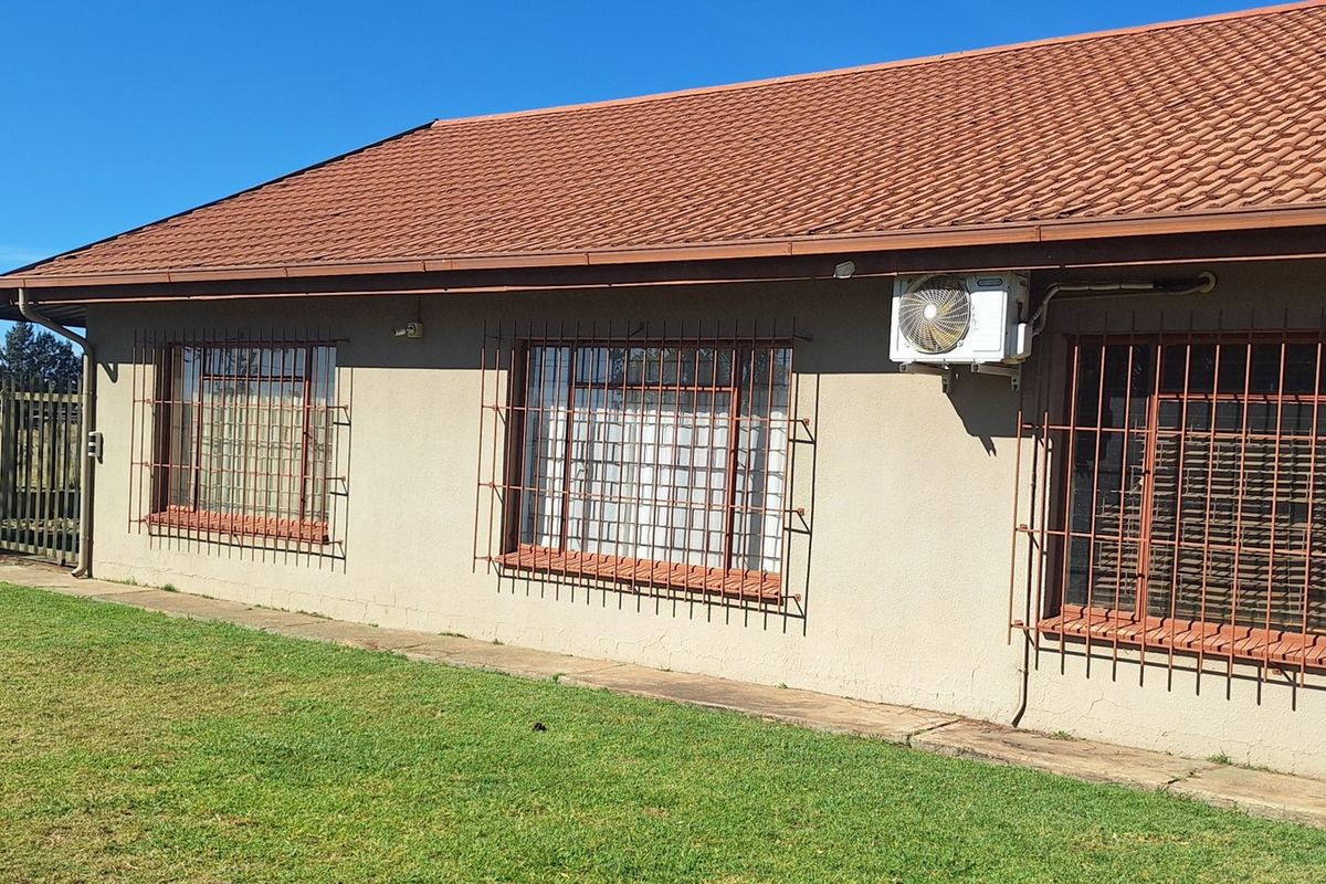 Rear exterior view of the property featuring a tiled roof, security bars on windows, an external air conditioning unit, and a surrounding lawn area.