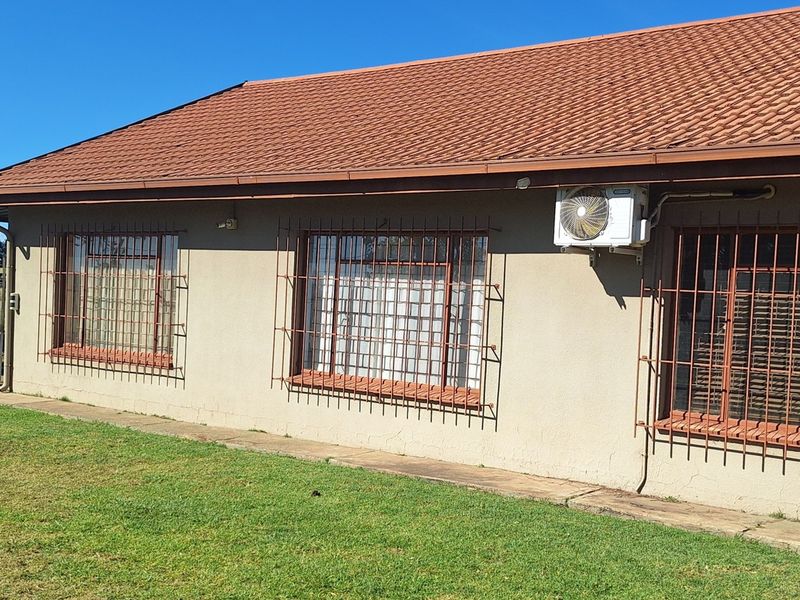 Rear exterior view of the property featuring a tiled roof, security bars on windows, an external air conditioning unit, and a surrounding lawn area.