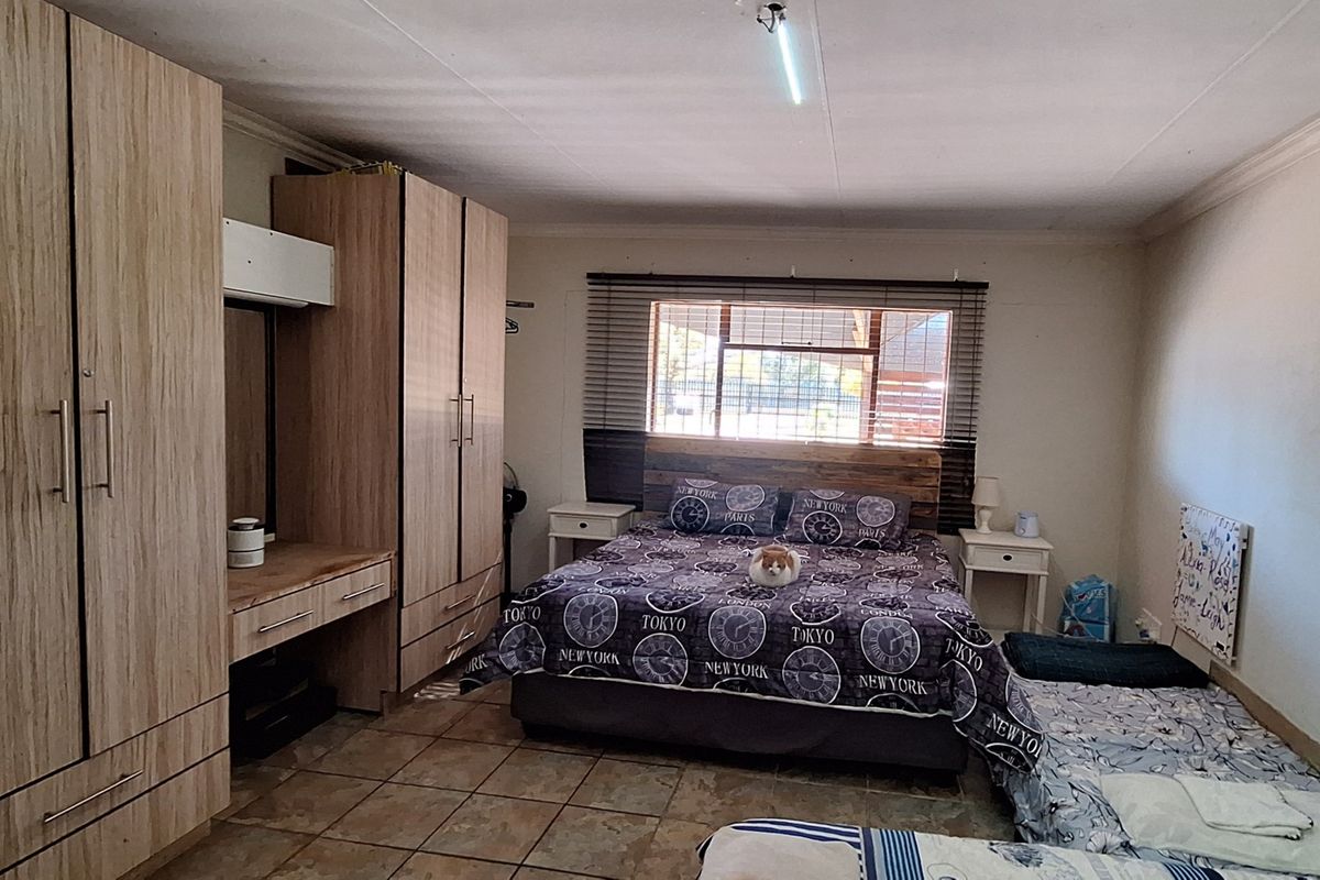 A spacious bedroom featuring built-in wooden cupboards, tiled flooring, and venetian blinds, offering a functional layout with ample storage space.