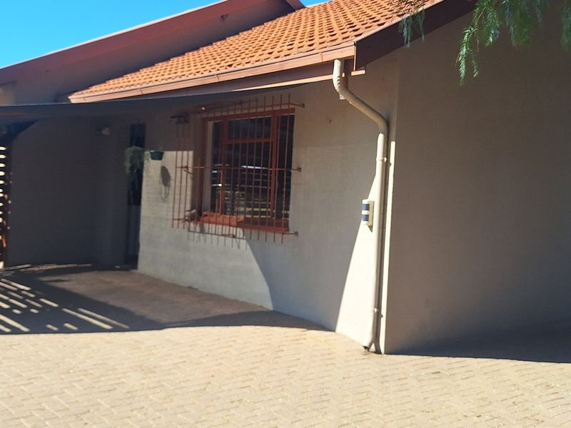 Front elevation of a small holding property featuring a tiled roof, paved driveway, and a covered carport area.
