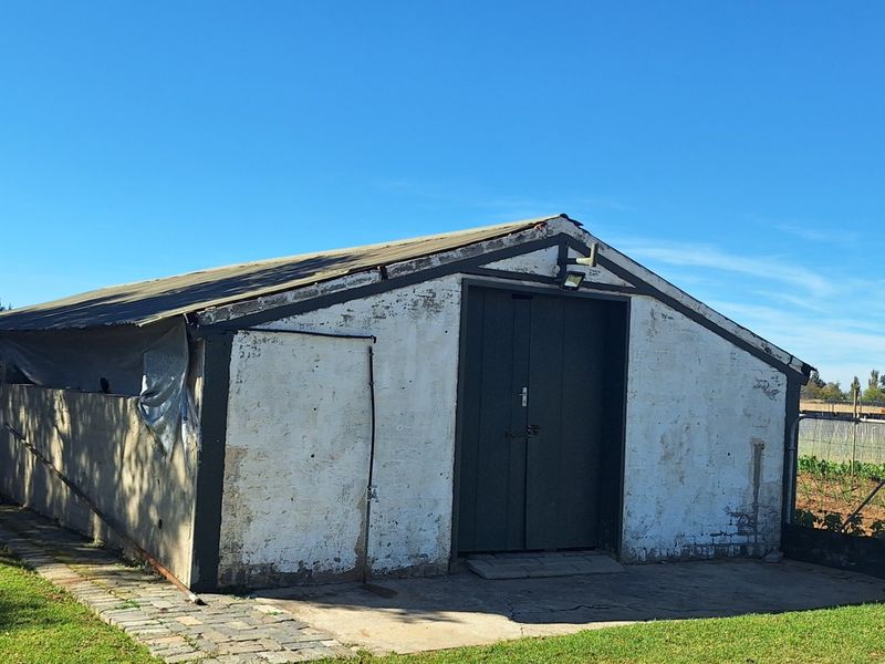 A detached utility outbuilding or storage shed featuring brick construction with a corrugated metal roof, situated on a small holding property.