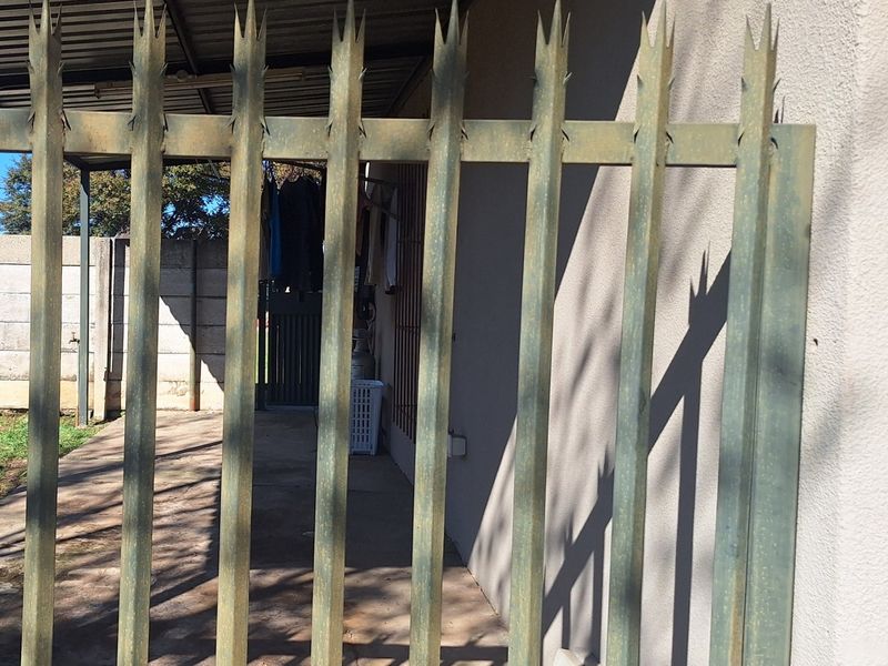 View of the rear exterior area featuring a metal spike security fence and a covered patio space.