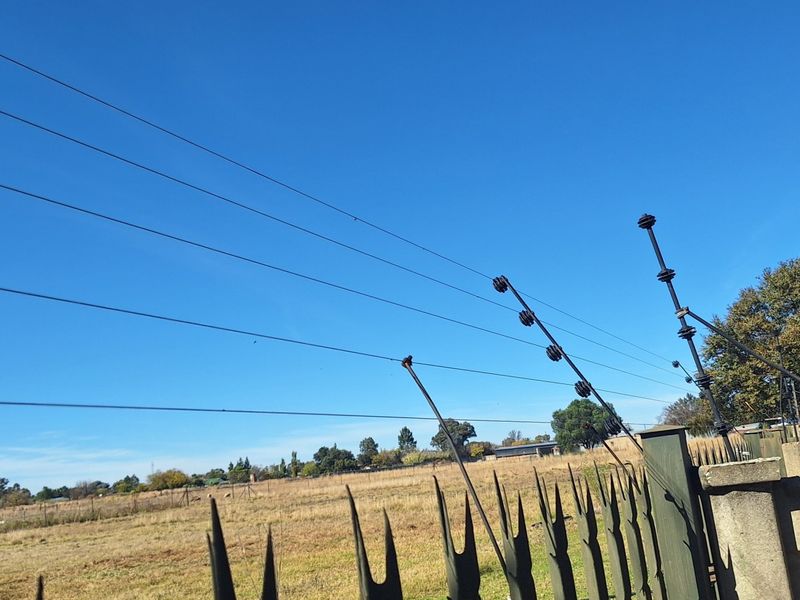 View of the property boundary featuring a concrete wall with spiked metal fencing and an integrated electric security fence overlooking open land.