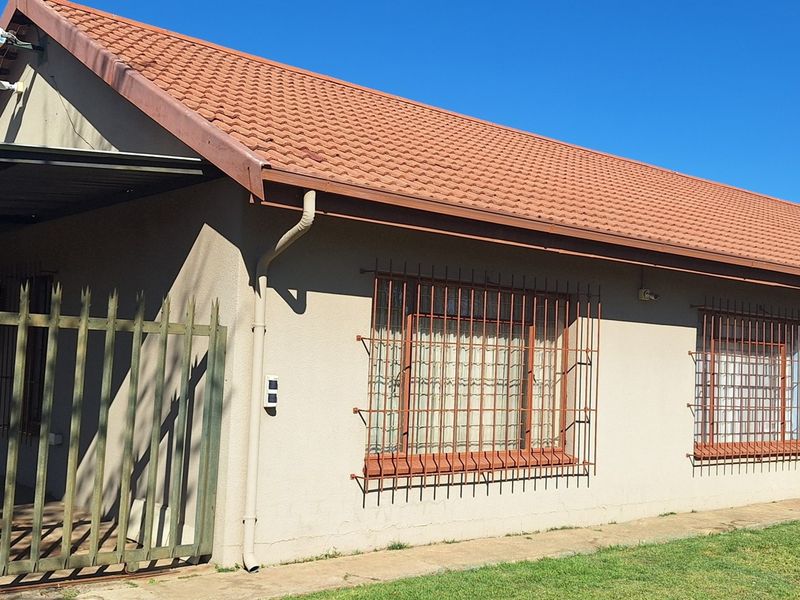 Front exterior view of a small holding property featuring a tiled roof, security bars on windows, and an attached carport.