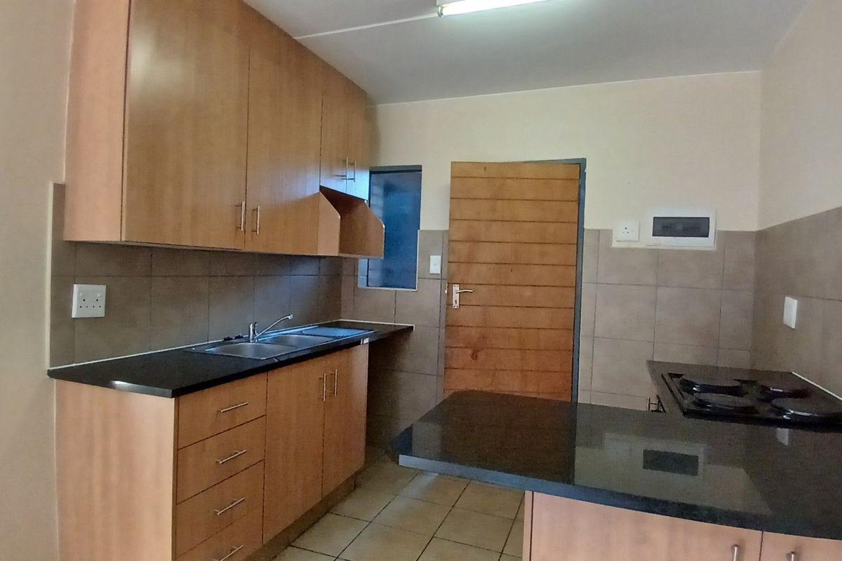 A functional kitchen featuring wooden cabinetry, granite countertops, a built-in hob, and tiled splashbacks, offering a clean and practical workspace.
