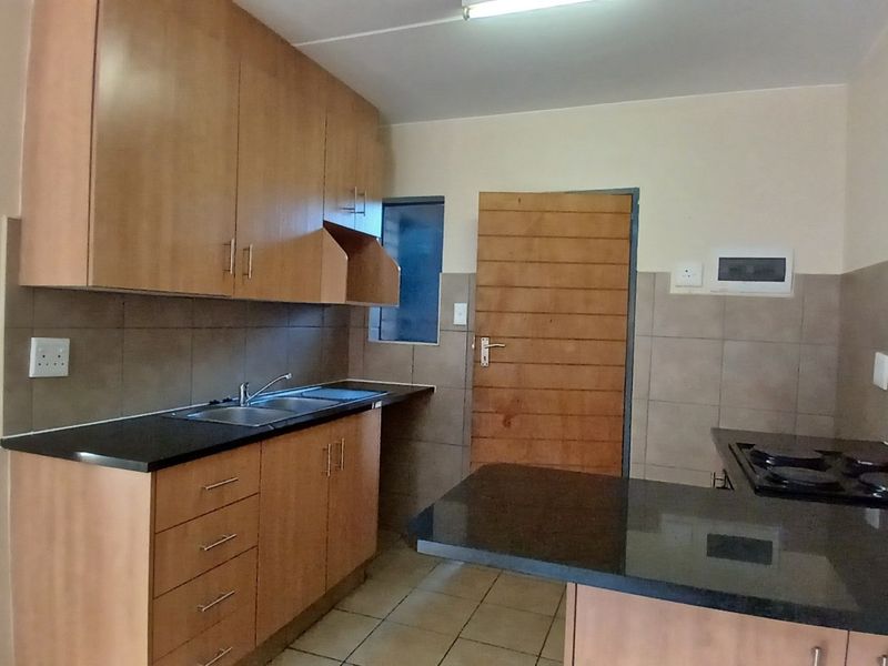 A functional kitchen featuring wooden cabinetry, granite countertops, a built-in hob, and tiled splashbacks, offering a clean and practical workspace.