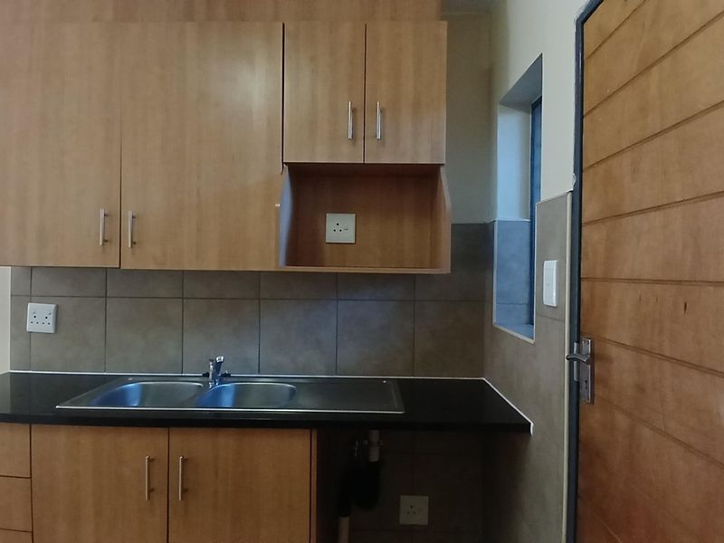 A clean, functional kitchen featuring laminate cabinetry, granite countertops, a double bowl stainless steel sink, and neutral tiled backsplash.