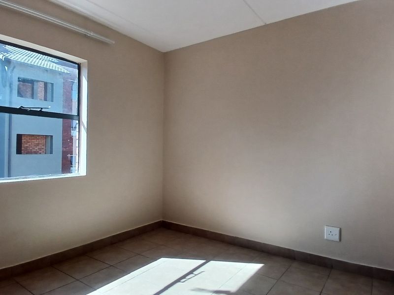 An empty bedroom featuring neutral wall paint, tiled flooring, and a window providing natural light.