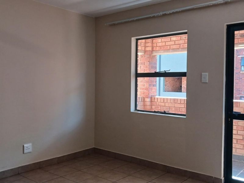 An empty bedroom featuring tiled flooring, neutral wall paint, and direct access to an exterior balcony through an aluminium door.