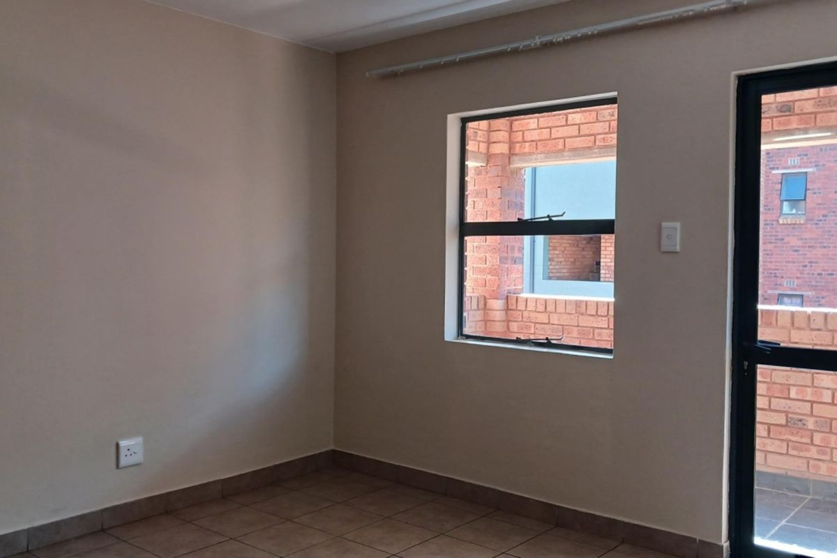 An empty bedroom featuring tiled flooring, neutral wall paint, and direct access to an exterior balcony through an aluminium door.