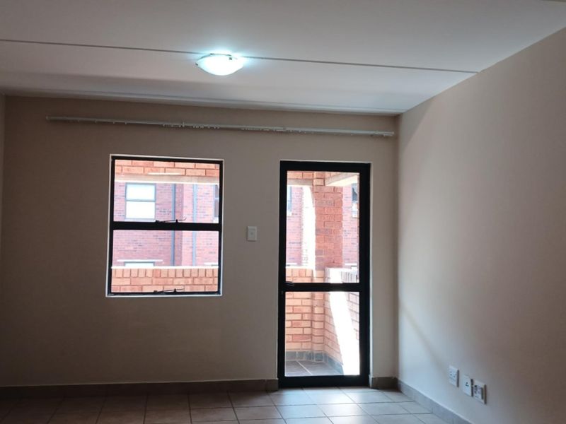 An empty living room featuring tiled flooring, neutral walls, and direct access to an outdoor patio area through an aluminium door.