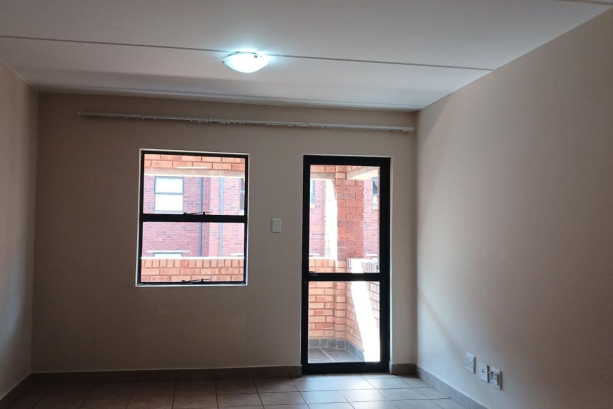 An empty living room featuring tiled flooring, neutral walls, and direct access to an outdoor patio area through an aluminium door.