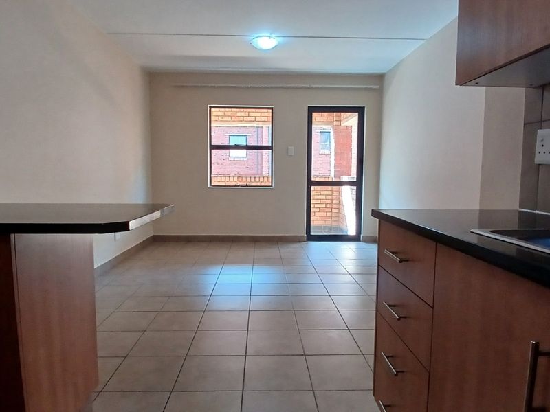 An open-plan living and kitchen area featuring tiled flooring, built-in cabinetry with dark countertops, and direct access to an outdoor space via a glass door.
