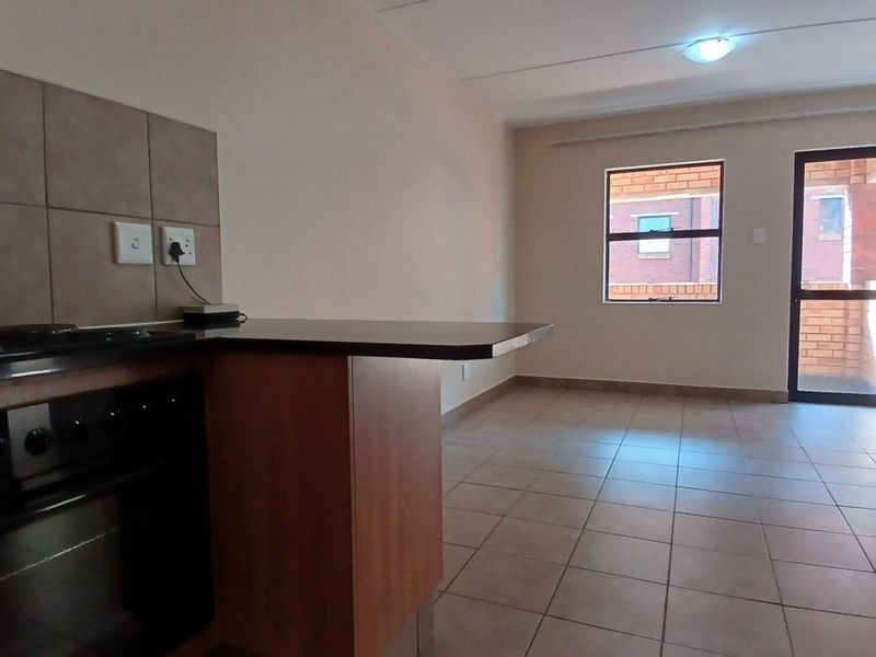 An open-plan kitchen and living area featuring tiled flooring, built-in cabinetry with a hob and oven, and access to an outdoor balcony area.