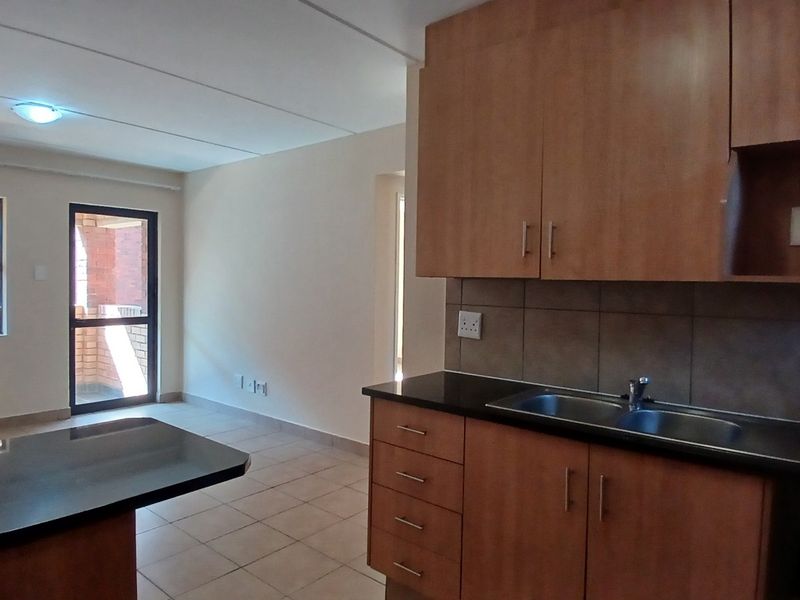 Open-plan kitchen and living area featuring wooden cabinetry, dark granite countertops, tiled flooring, and access to a balcony through a sliding glass door.