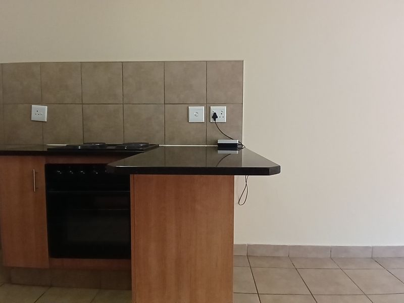 A compact kitchen area featuring built-in cabinetry, a dark granite countertop, an integrated oven and hob, and neutral tiled finishes.