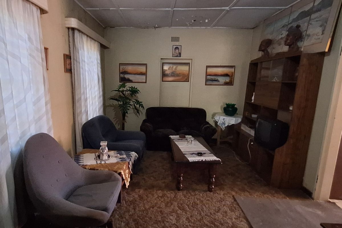 A dated living room featuring a built-in shelving unit and original ceiling tiles, requiring cosmetic updates to modernize the space.