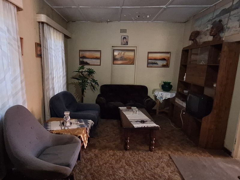 A dated living room featuring a built-in shelving unit and original ceiling tiles, requiring cosmetic updates to modernize the space.