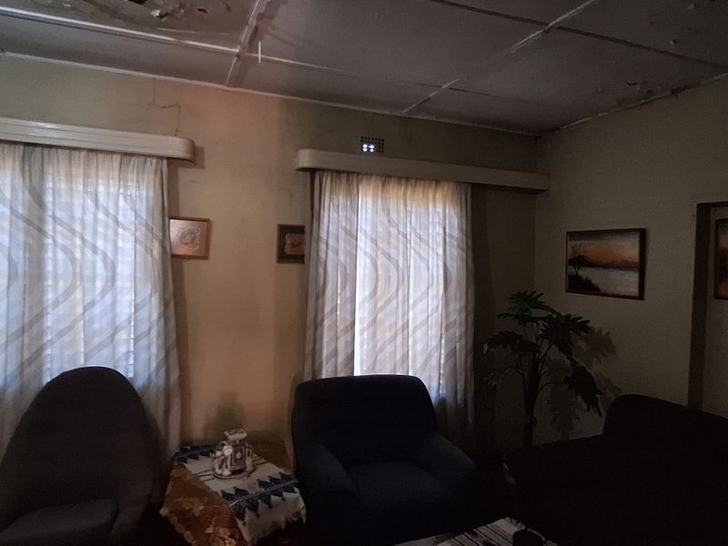 A dimly lit living room featuring visible ceiling damage and wall cracks, requiring maintenance and cosmetic updates to improve the overall condition.
