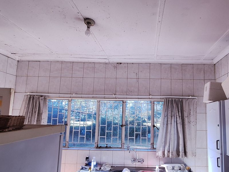 A dated kitchen featuring original cabinetry, tiled splashbacks, and metal-framed windows with security bars, requiring significant renovation and cosmetic updates.