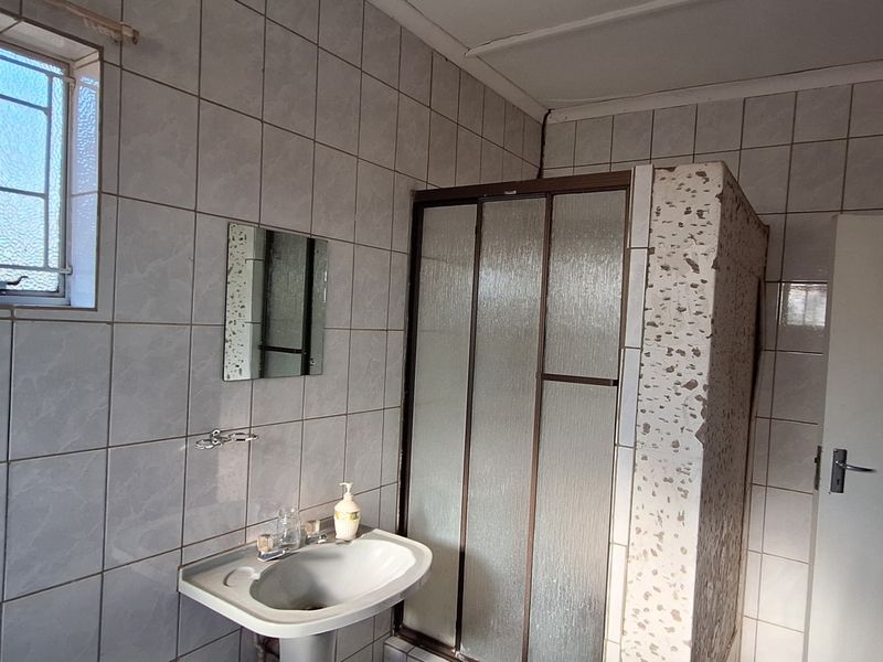 A functional bathroom featuring a pedestal basin and a shower enclosure, requiring some cosmetic repairs to the wall finishes and shower surround.