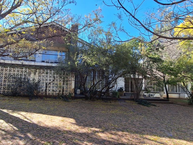 Rear view of the property featuring a paved courtyard, mature trees, a balcony, and decorative breeze block architectural elements.
