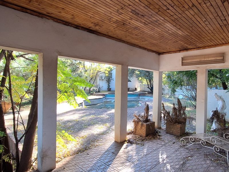 A covered patio area featuring a timber ceiling and paved flooring, overlooking a swimming pool and garden area.