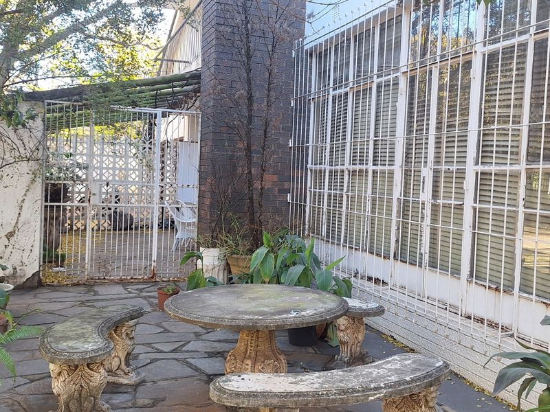 Outdoor patio area featuring stone paving, a brick chimney, and security-barred windows, offering a private space for outdoor relaxation.