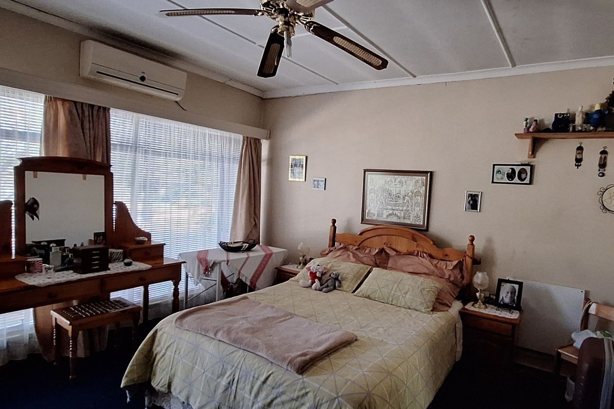A well-lit bedroom featuring a ceiling fan, split-system air conditioning unit, and large windows with venetian blinds.