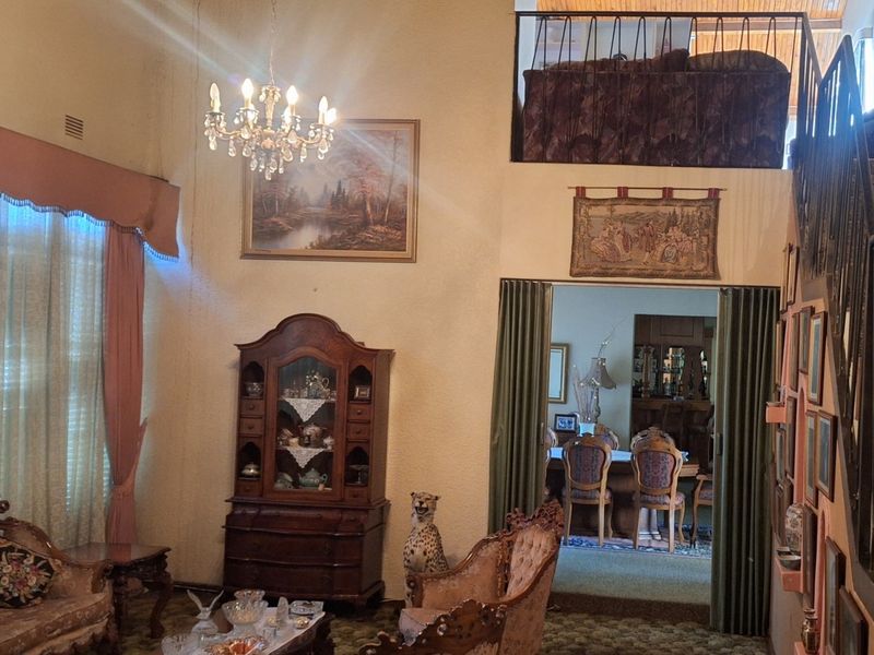 Spacious living room featuring a vaulted ceiling, a staircase leading to a mezzanine level, and a classic chandelier, offering significant potential for modernization.