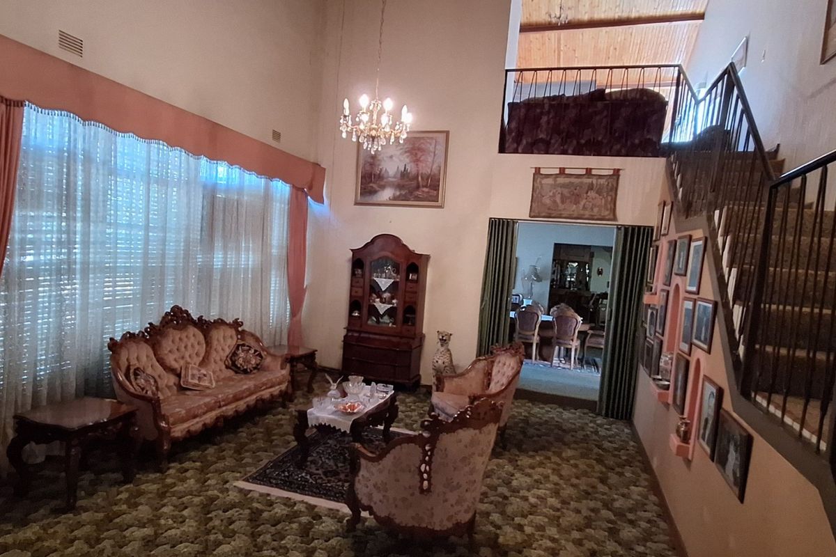 Spacious double-volume living room featuring a mezzanine level, exposed timber ceiling beams, and a staircase with metal railings.