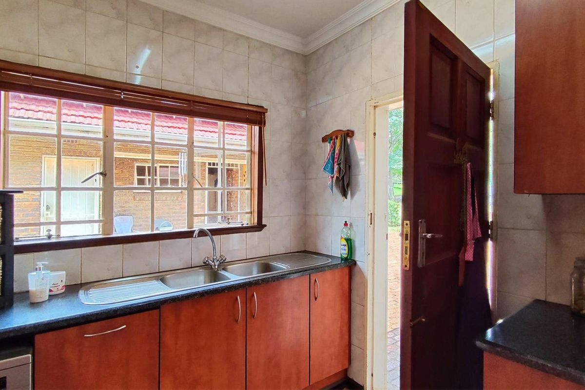 A functional kitchen area featuring wooden cabinetry, laminate countertops, a double basin sink, and tiled wall finishes with direct access to the exterior.