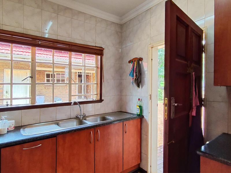 A functional kitchen area featuring wooden cabinetry, laminate countertops, a double basin sink, and tiled wall finishes with direct access to the exterior.
