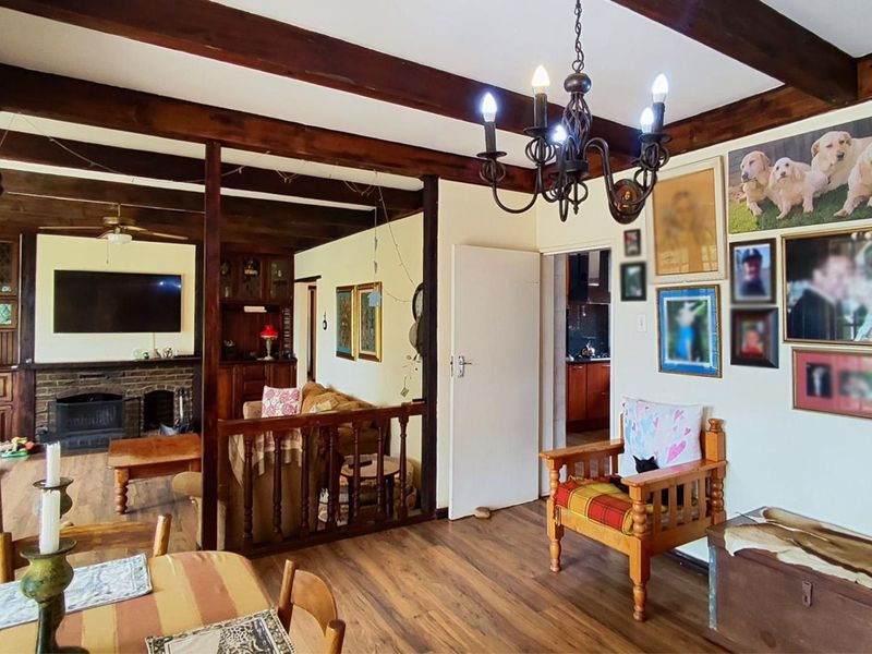Spacious open-plan living area featuring exposed timber ceiling beams, a brick fireplace, and warm timber flooring, creating a rustic and inviting atmosphere.