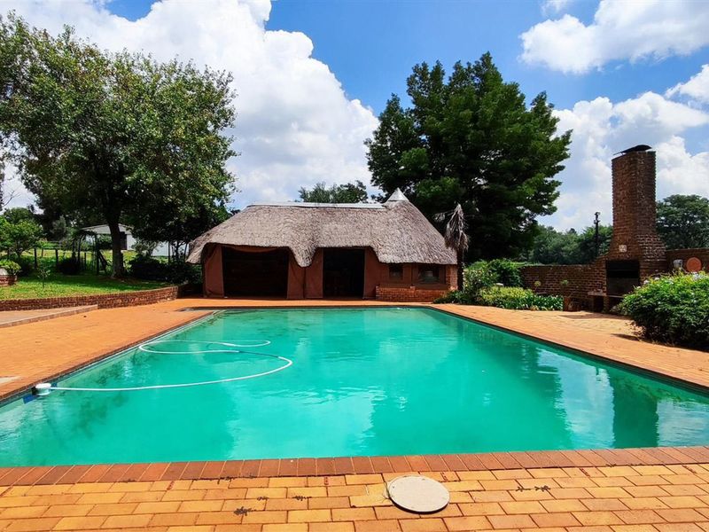 Outdoor pool area featuring a large swimming pool, brick paving, and a traditional thatched lapa with an integrated brick fireplace.